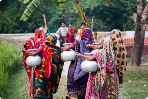Women carrying water jugs in a rural area